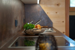 Kräuter und ein Apfel auf der Arbeitsfläche einer Küche. Im Vordergrund sieht man die Kochplatte.