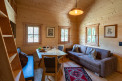 slider-11 Innenansicht eines Hauses, mit Sitzgruppe und Sofa. Drei Fenster. Aufgang zum Hochbett auf der linken Seite.