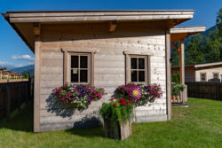 slider-12 Seitenansicht eines Holzhauses mit zwei Fenstern. Blumentröge hängen unter den Fenstern.