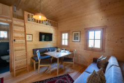 slider-4 Ansicht einer Hütte von innen, mit Fenstern, Lampe, Hochbett, Sitzecke und Sofa.